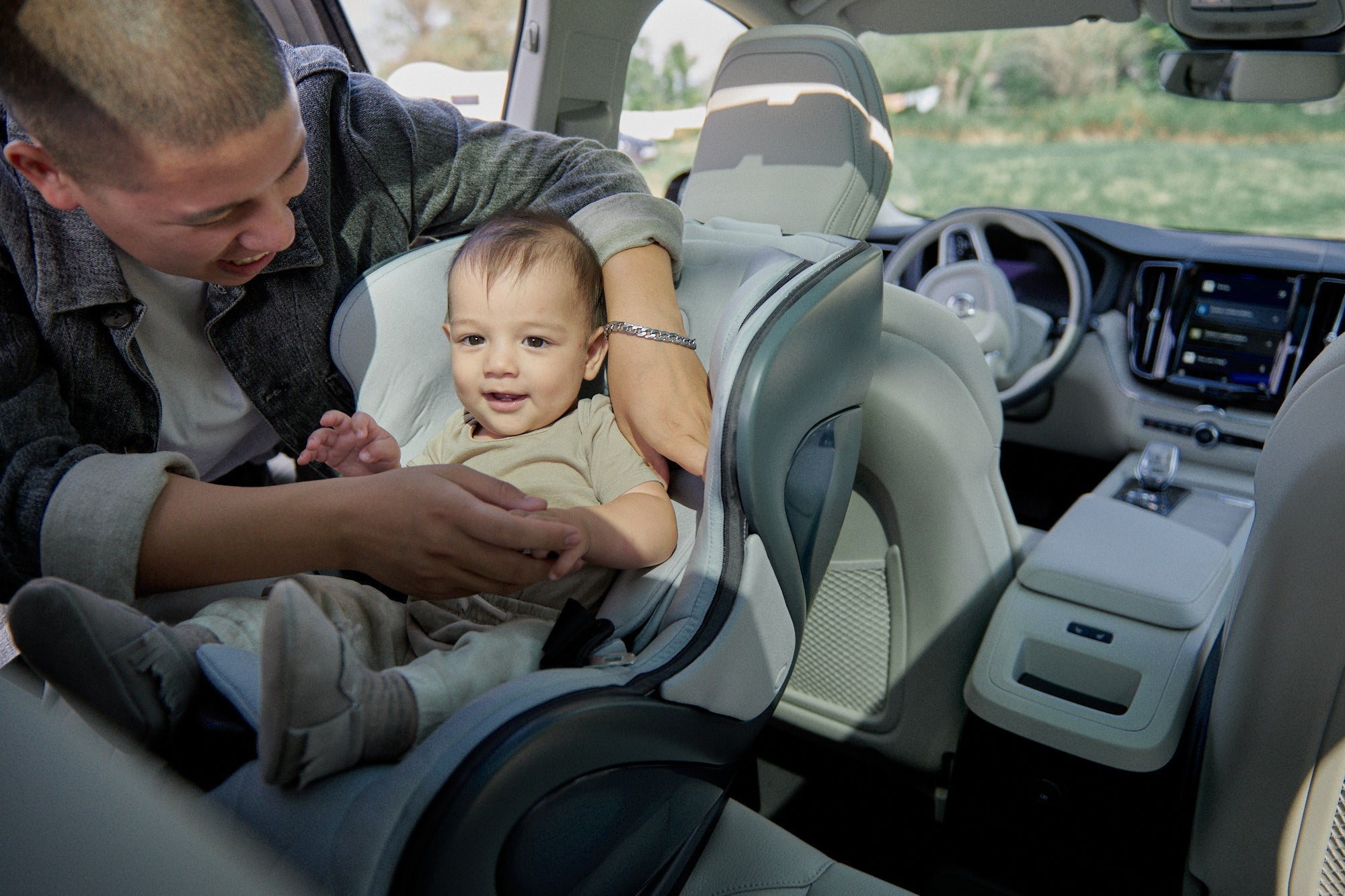 a father or male caretaker buckles the babyark convertible car seat harness on his smiling child, rear facing in a luxury car