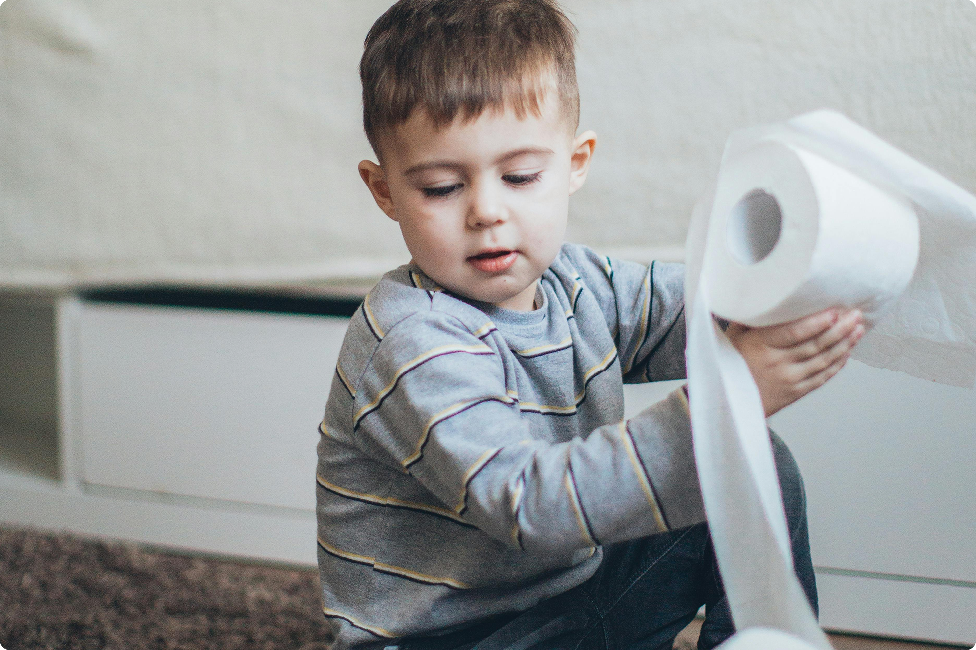 little boy potty training and playing with rolls of toilet paper as part of potty training process